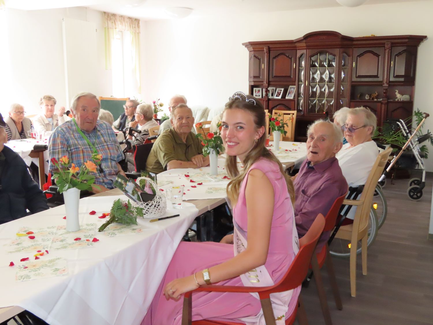 die Rosenkönigin sitzt mit Bewohner*innen am Tisch