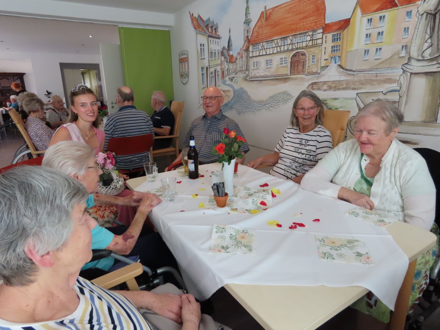 die Rosenkönigin sitzt mit Bewohner*innen am Tisch