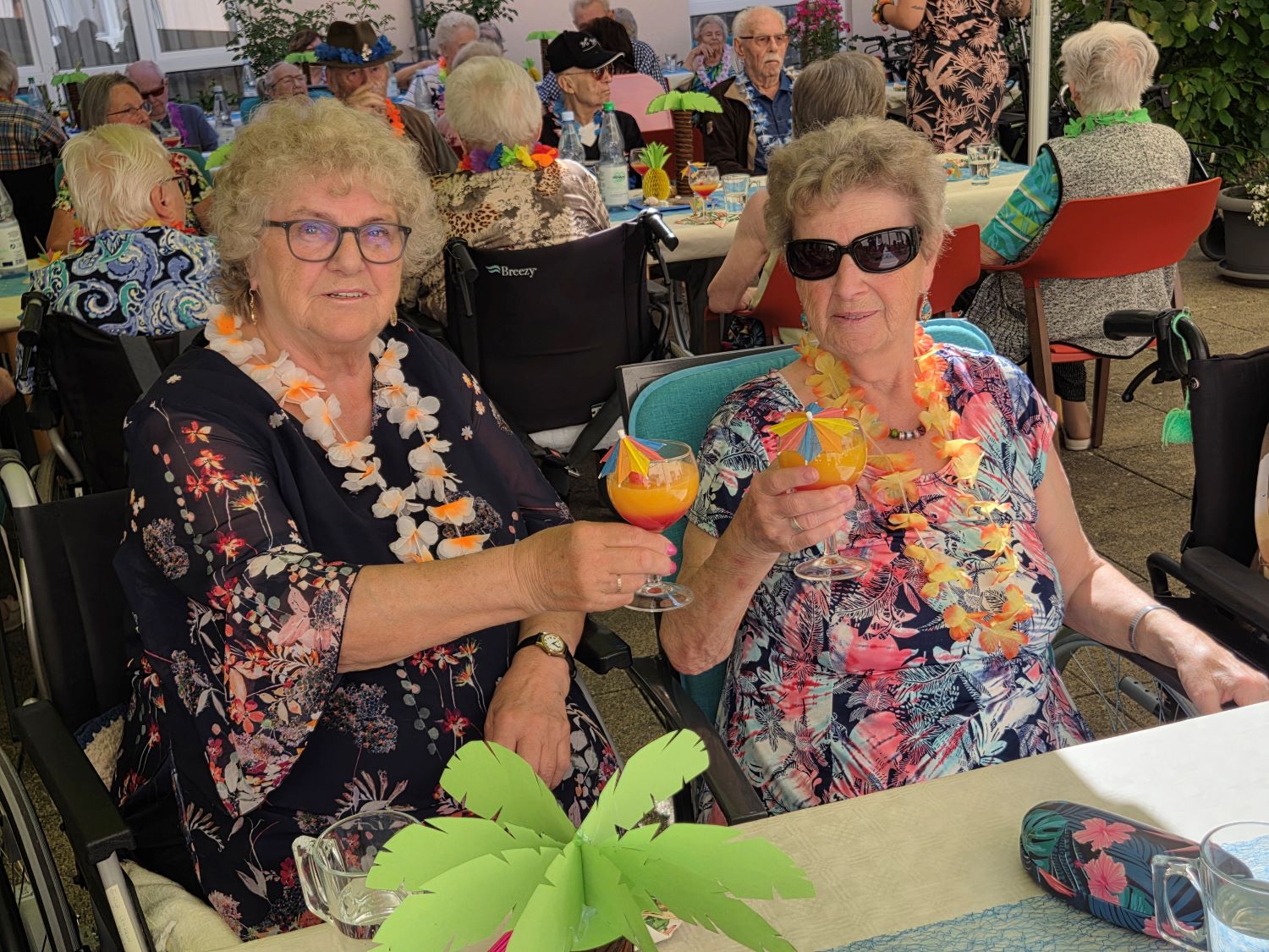 die Bewohner*innen sitzen in gemeinsamer Runde am Tisch und trinken Cocktails
