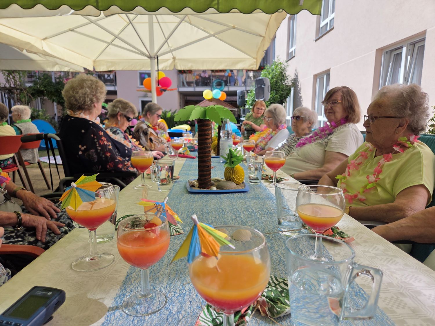 die Bewohnerinnen sitzen in gemeinsamer Runde am Tisch und trinken Cocktails