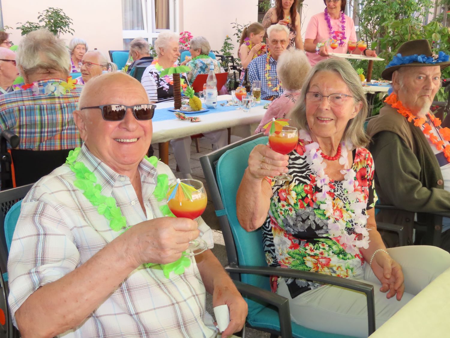 die Bewohner*innen sitzen in gemeinsamer Runde am Tisch und trinken Cocktails