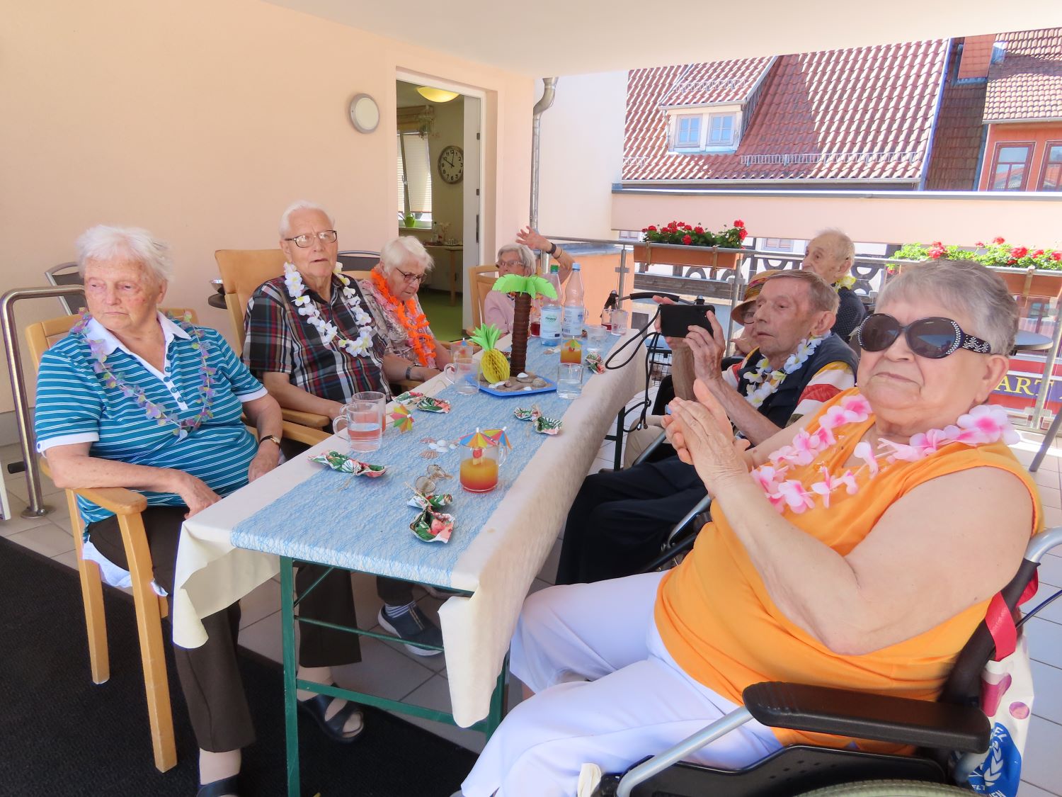 die Bewohner*innen sitzen in gemeinsamer Runde am Tisch und trinken Cocktails